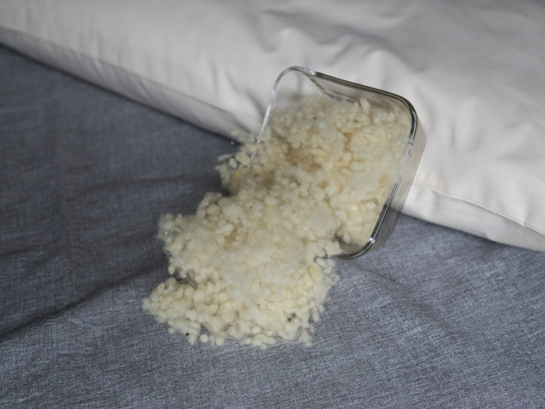 Schafswolle in Glasschüssel an ein Körnerkopfkissen angelehnt. Schafswollefüllung für Körnerkopfkissen.