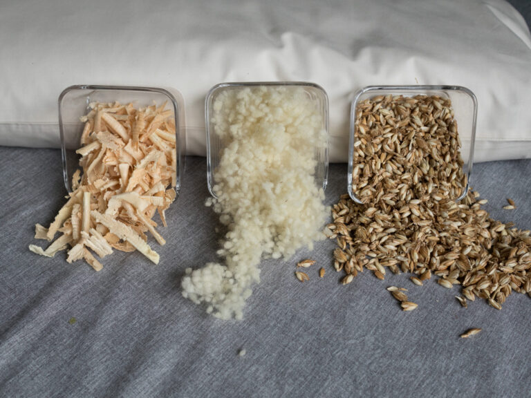 Dinkelspelzen, Schafswolle und Zirbenspäne in Glasschüsseln an ein Körnerkopfkissen angelehnt. Dinkelfüllung, Schafswollefüllung und Zirbenfüllung für Körnerkopfkissen.