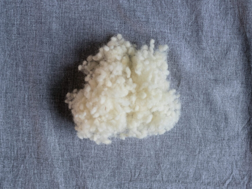 Schafswollflocken als Füllung für Körnerkissen als Nahaufnahme auf grauem Hintergrund