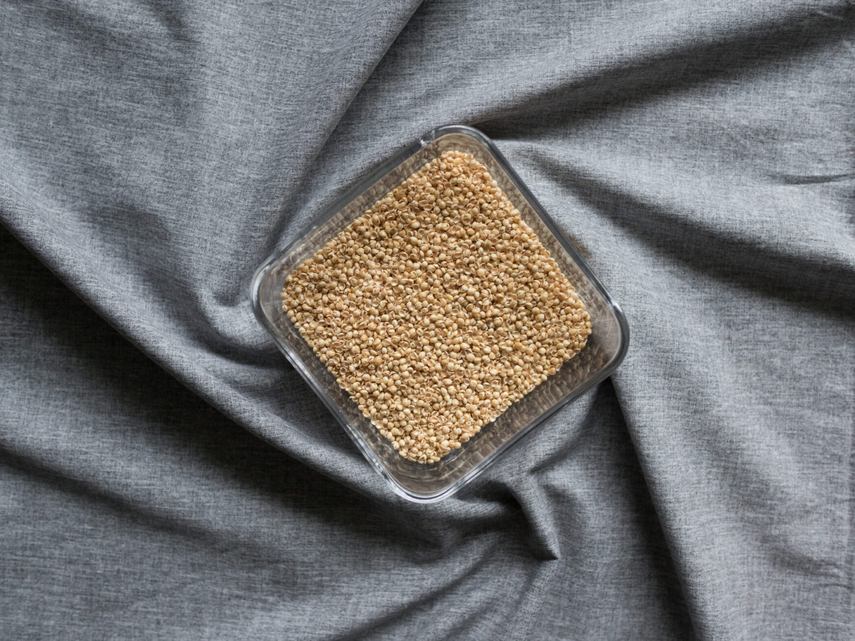 Hirseschalen in Glasschüssel für Körnerkopfkissen auf grauem Hintergrund.