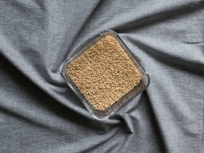 Hirseschalen in Glasschüssel für Körnerkopfkissen auf grauem Hintergrund.