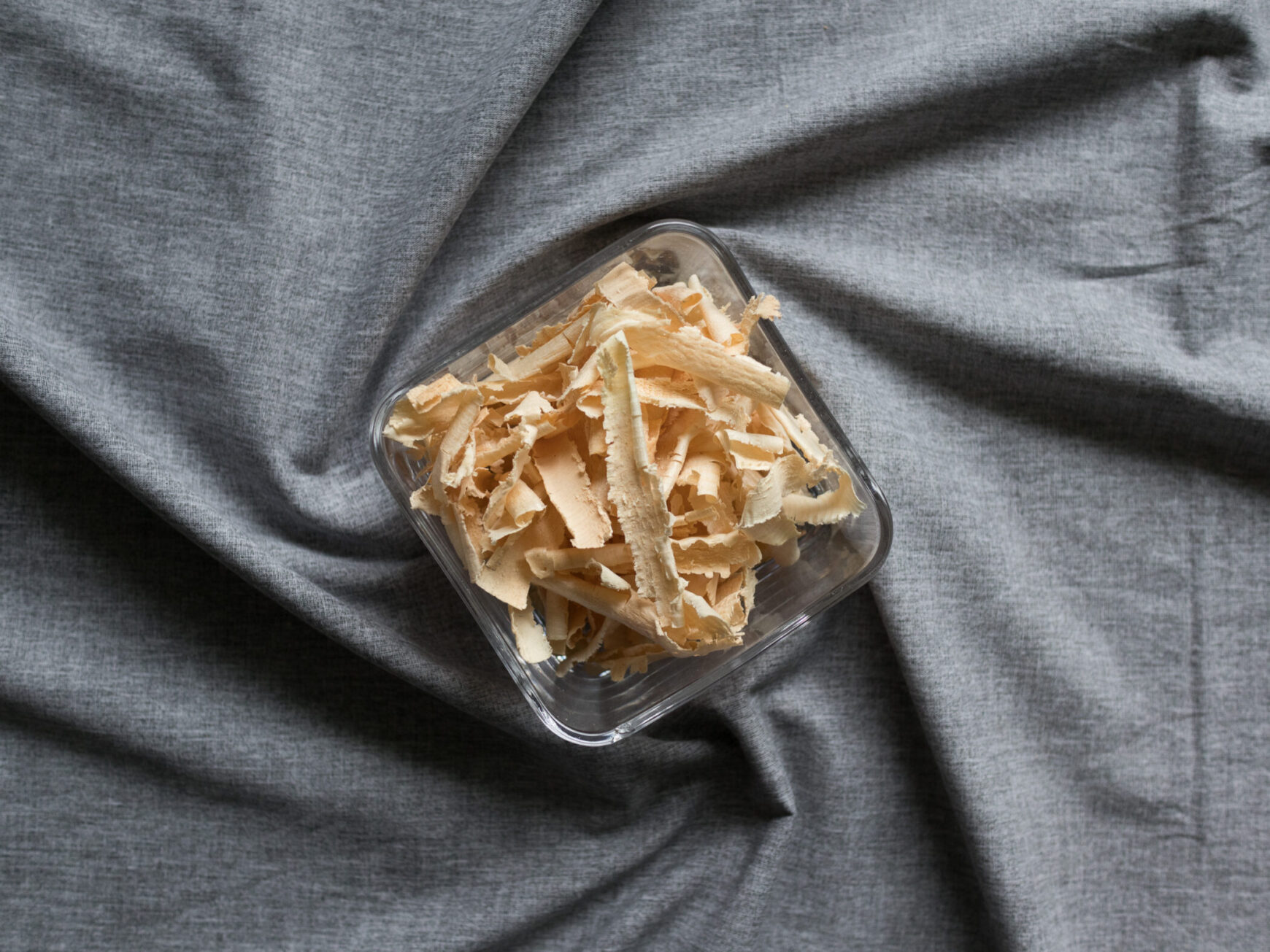 Zirbenspäne in Glasschüssel für Körnerkopfkissen auf grauem Hintergrund.