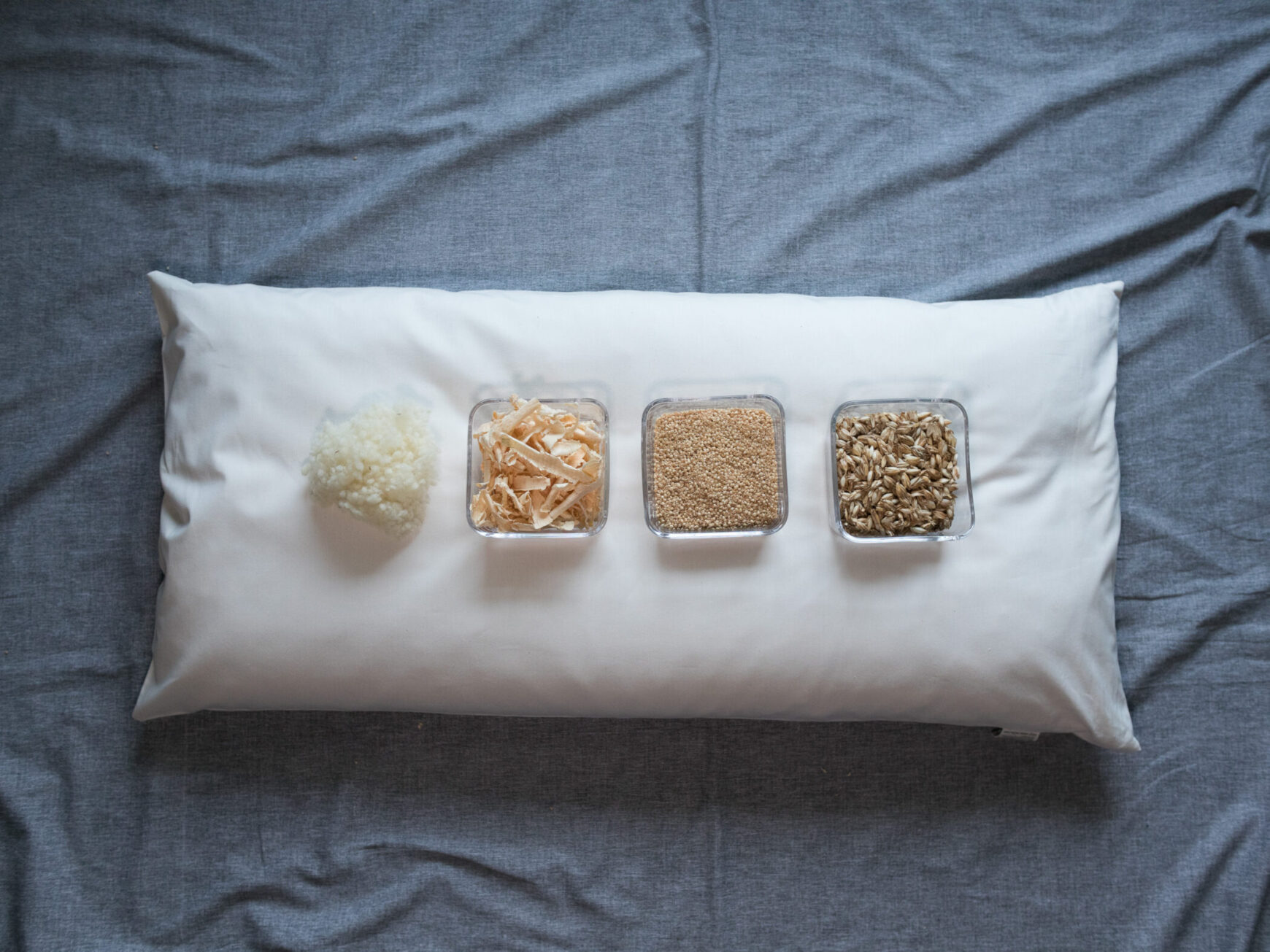 Körnerkopfkissen in natürlichem Licht auf grauem Hintergrund. Zirbenspäne, Hirseschalen, Dinkelspelzen und Schafswolle sind in Glasschüssel auf dem Kissen