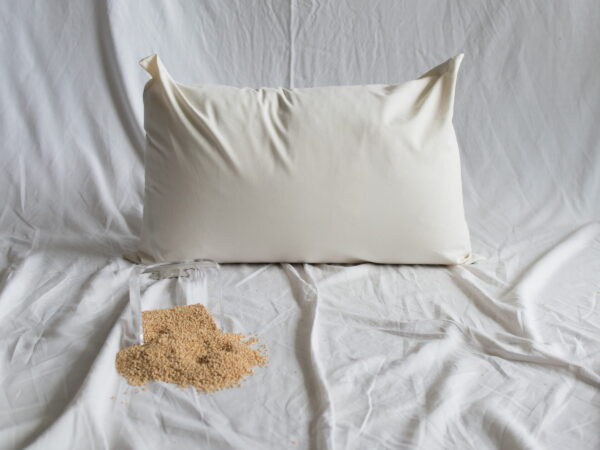 Hirsekopfkissen von Kissenkorner auf weißem Bettlaken. Vor dem Kissen steht eine Schüssel mit Hirseschalen.