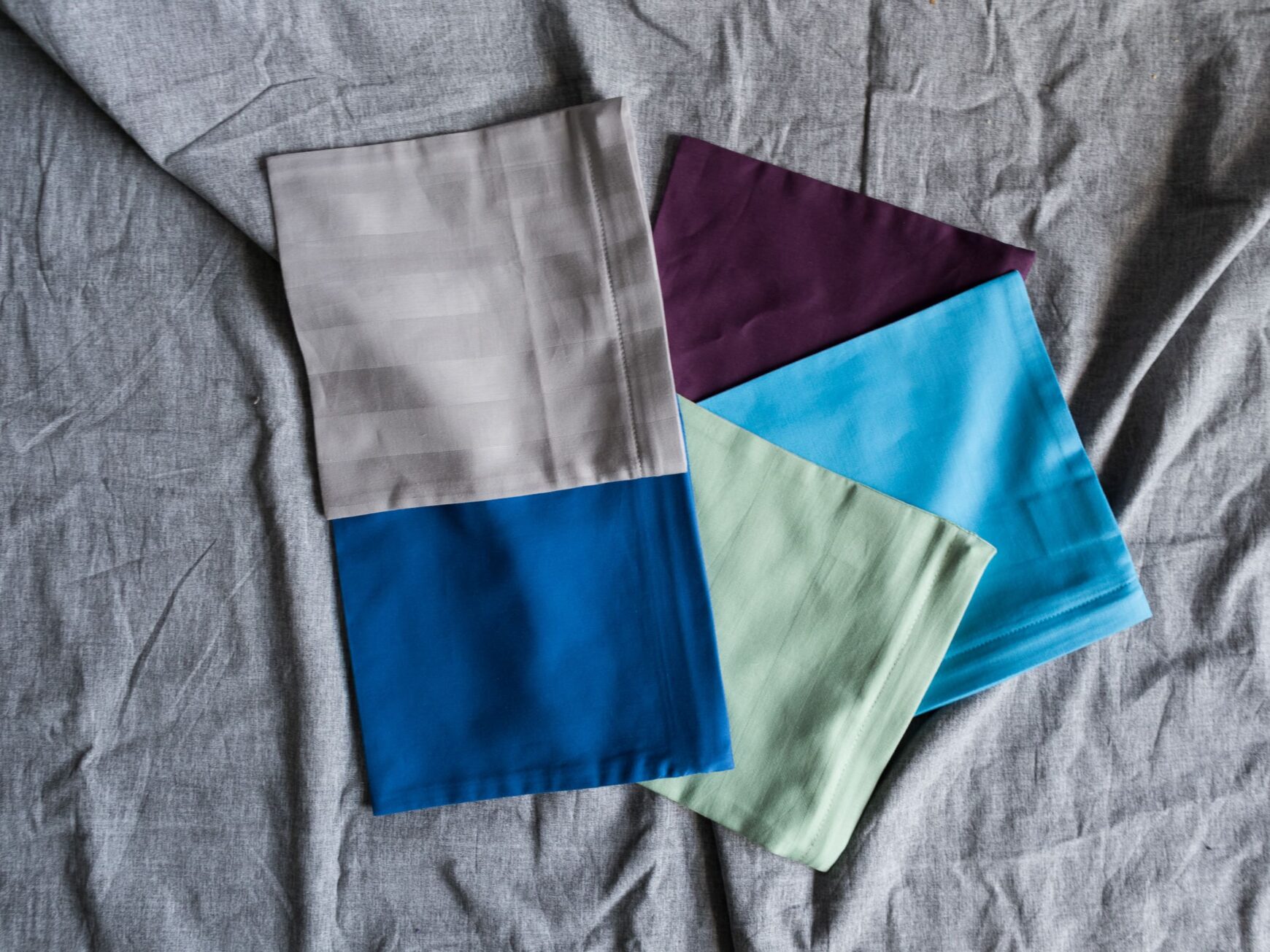 Kissenkorner Wärmekissen-Bezüge in mehreren Unifarben gefächert: Grau gestreift, Aubergine, Hellblau, Mint und Blau