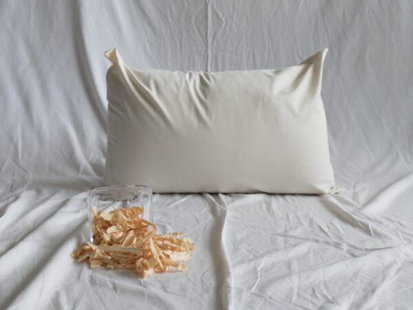 Zirbenkopfkissen von Kissenkorner auf weißem Bettlaken. Vor dem Kissen steht eine Schüssel mit Zirbenspänen.